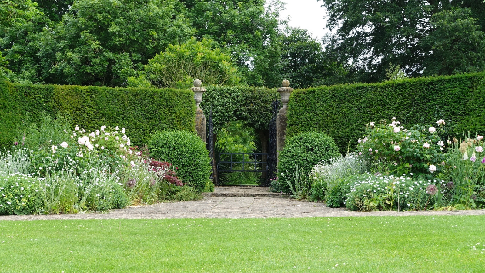 A formal garden featuring green arches and symmetrical pathways, with orderly, trimmed shrubs and flourishing flower beds in a classic design.