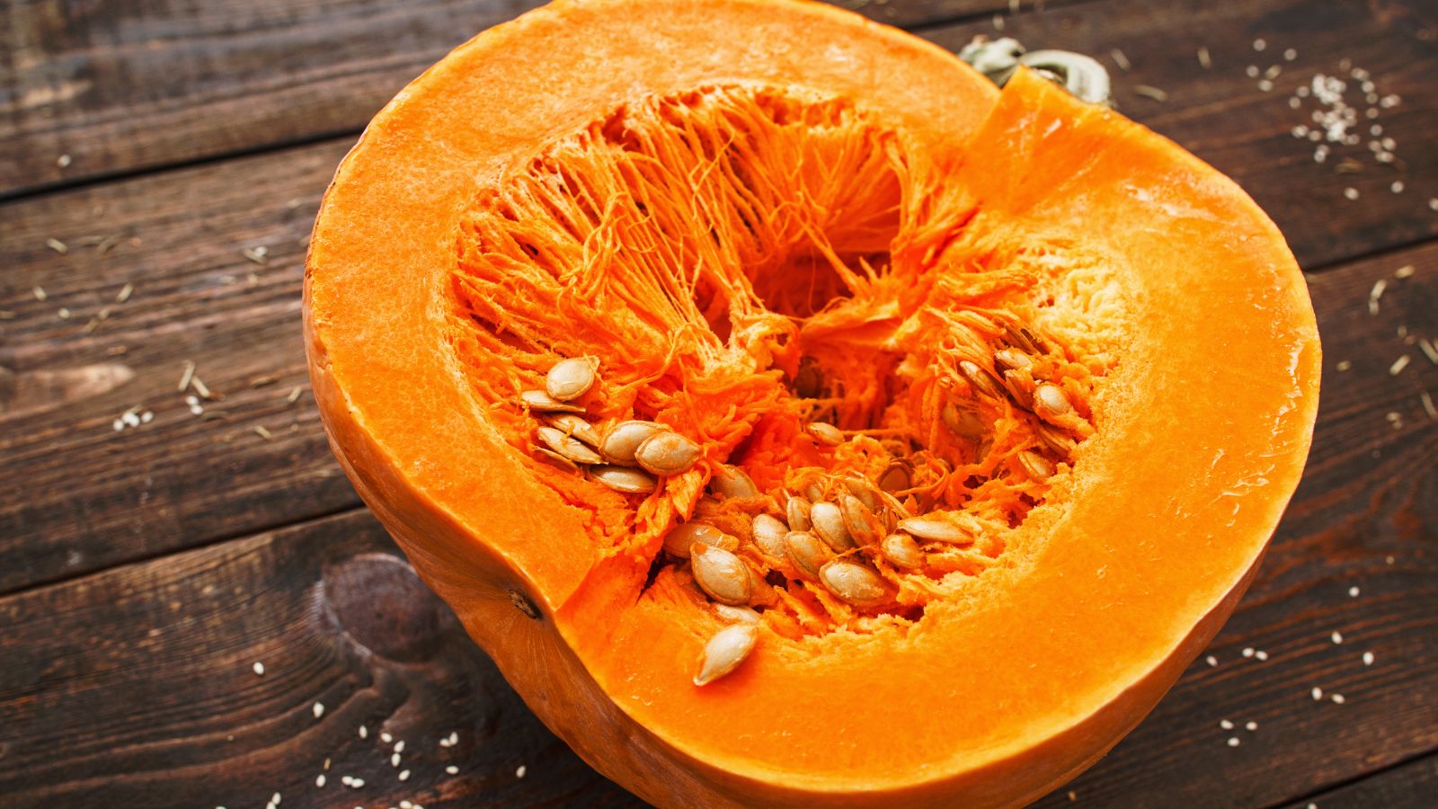 A focused shot of a round orange vegetable crop that is sliced in half showcasing its organic matter on a wooden surface.